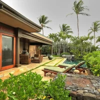 A luxurious outdoor patio area with lounge chairs, surrounded by lush greenery and palm trees, leading to a pool.
